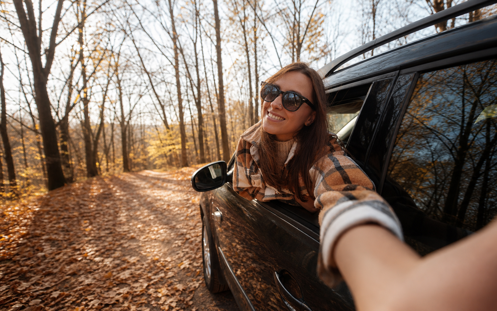 Junge Fahrerin lehnt sich auf einer herbstlichen Straße aus ihrem Auto